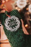 Clear acrylic stocking tags laser engraved with an evergreen wreath and a first name.  They are tied with a suede cord and sitting on top of festive red and green stockings.