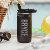 Black color 12-ounce stainless steel, flip-top straw tumbler. The tumbler is laser engraved and personalized with the name of the child, the font is in a simple block style. The tumbler is sitting on a white table with a yellow pool floaty in the background.