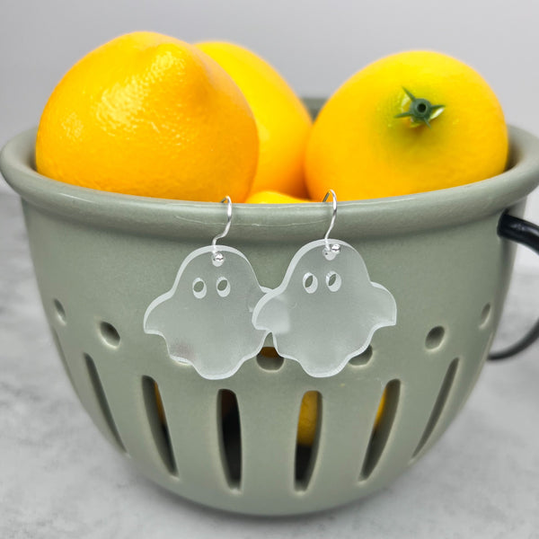a pair of frosted ghost earrings hanging on a green container with lemons