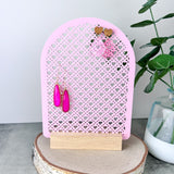 Pink Acrylic Earring Holder with heart shaped Rattan design on a light wooden base wih earrings hanging on it.  