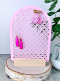 Pink Acrylic Earring Holder with heart shaped Rattan design on a light wooden base wih earrings hanging on it.