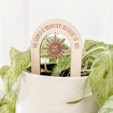 Arch-shaped wooden plant stake placed in a white planter with green pothos leaves. The stake is engraved with the phrase “The world is brighter because of you” and features a hanging sun-shaped charm engraved with “Love, Miles.”