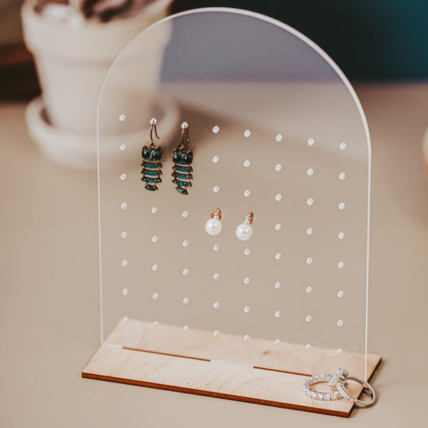 Clear acrylic earring holder freestanding with two pairs of earrings hanging and rings laying beside