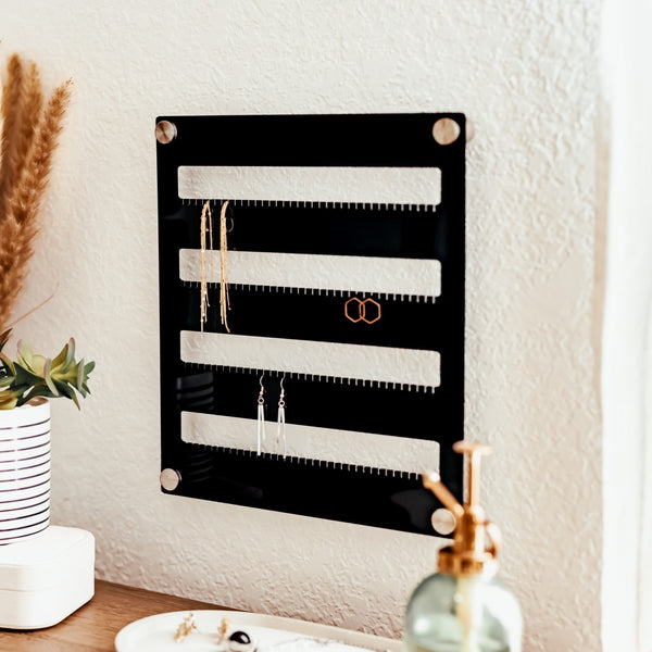 Shiny black acrylic earring holder hanging on a textured wall with silver hardware displaying three pairs of earrings