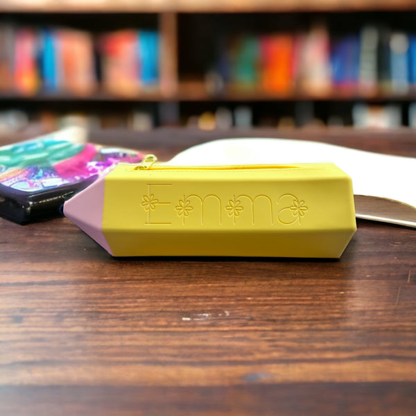 One personalized Yellow Pencil pouch sitting on a wooden desk with colorful books in the background