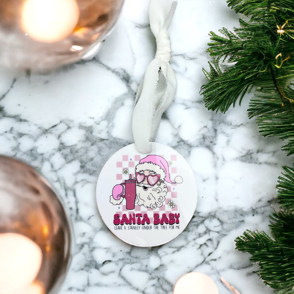 Round White ornament with Santa Baby, Leave a stanley Under the tree for me printed under a picture of a santa claus with pink heart shaped sunglasses and a 40 oz tumbler