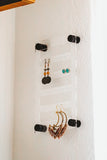 6 inch by 10 inch clear acrylic earring holder hanging on the wall with black screws and several pairs of earrings by legacy and Light