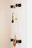 Side view of 6 inch by 10 inch clear acrylic earring holder hanging on the wall with black screws and several pairs of earrings by legacy and Light