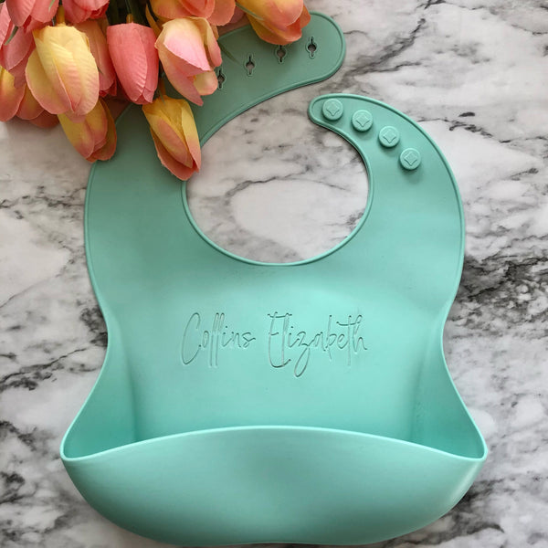 Silicone baby bib (Mint) with personalized name laser engraved in the center of the bib. The bib has a food catching pocket to help keep the baby and highchair free from mess. 