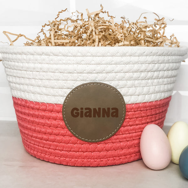 Pink and white braided Easter basket with engraved leather patch with the name Gianna with kraft basket filler and 3 colored eggs in the foreground