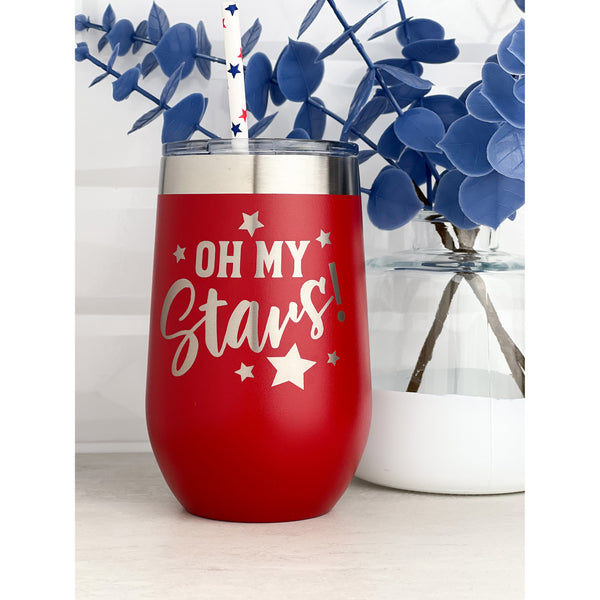 Red stainless steel  wine tumbler with 'Oh my stars' laser engraved for Fourth of July  with blue plant in the background with white glass vase