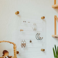 Clear acrylic earring organizer with gold hardware shown with several pairs of earrings of different styles