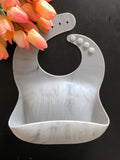 Marbled patterned (white and gray) personalized silicone baby bib. Personalized with laser engraved name across the front. Bib has a food catching pocket to keep baby and highchair mess free.