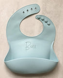 Sage baby silicon bib personalized laser engraved name across the front of the bib. The bib has a food catching pocket to help keep baby and highchair mess free.