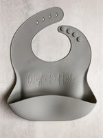 Gray baby silicon bib personalized laser engraved name across the front of the bib. The bib has a food catching pocket to help keep baby and highchair mess free.