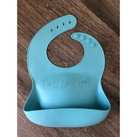 Blue silicone toddler bib engraved with I'm a sweet one! on a wooden background by Legacy and Light