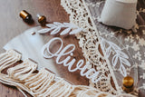 close-up showing detail of the hair bow holder. Showing the raised name and leaf details. The hair bow holder is stiting on a wood table with lace accents.