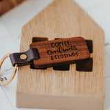 Dark stained wood keychain close up showing detail of the laser engraved "Coffee, Contracts & Closing" on the front. Gold colored keyring is secured to the wood keychain by a vegan leather strap secrured with a gold colored metal stud. 